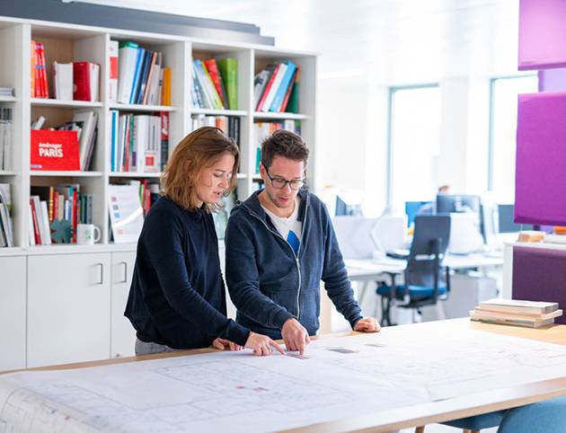 Zwei Mitarbeitende von Artelia arbeiten im Büro gemeinsam an einem Baugrundriss